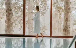 Frau im Bademantel am Pool mit Blick in die Natur.