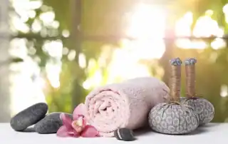 Wellnessarrangement mit Handtuch, Massagesteinen und Akupunkturnadeln.
