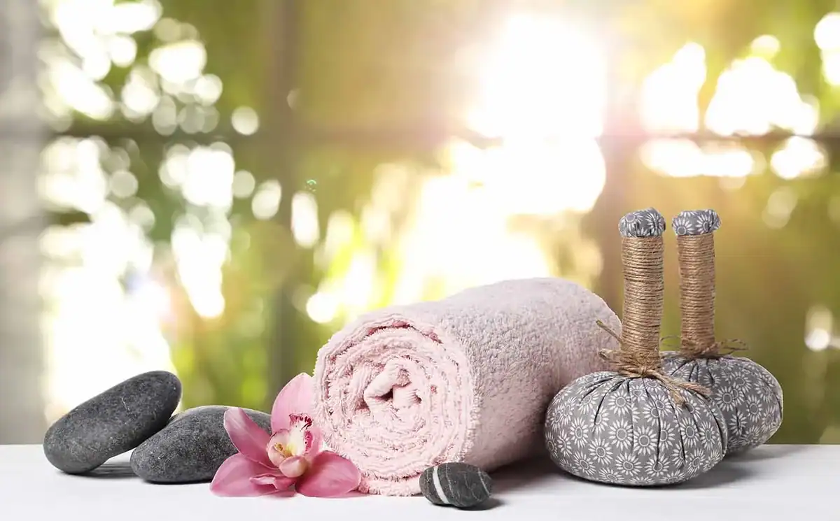 Wellnessarrangement mit Handtuch, Massagesteinen und Akupunkturnadeln.