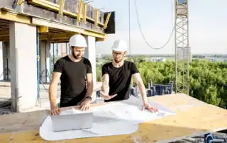 Zwei Fachplaner besprechen Baupläne auf einer Baustelle.