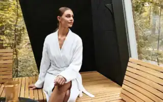 Frau im Bademantel entspannt in einem naturnahen Wellnessbereich.