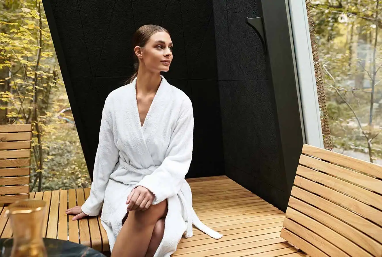 Frau im Bademantel entspannt in einem naturnahen Wellnessbereich.