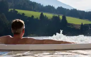 Mann entspannt im warmen Aussenpool mit Blick auf die Berglandschaft.