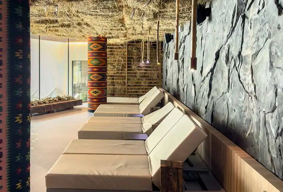 Ruheraum mit Relaxliegen und Natursteinwand.