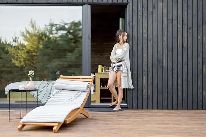 Frau entspannt auf einer Terrasse vor einem modernen Wellnessbereich.