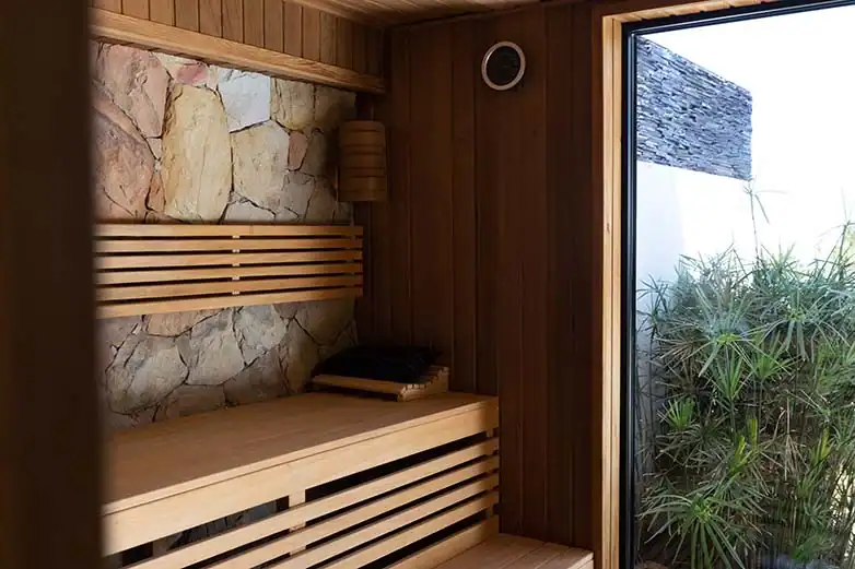 Moderner Wellnessbereich mit Holzsauna, Natursteinwand und Fensteröffnung ins Grüne.